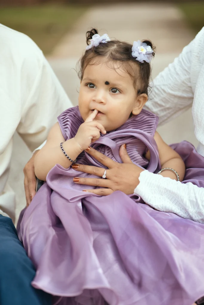 Baby girl sitting on her parent's lap wearing a lavender party dress.