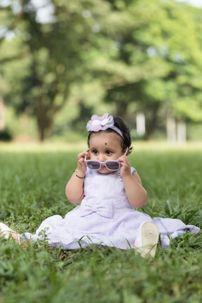 Cute toddler wearing sunglasses while sitting on the grass in a playful portrait.