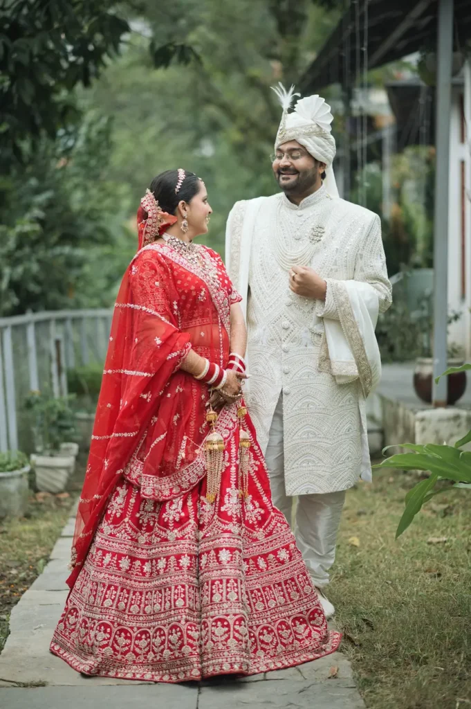 Newlywed couple walking together in traditional wedding attire surrounded by greenery.