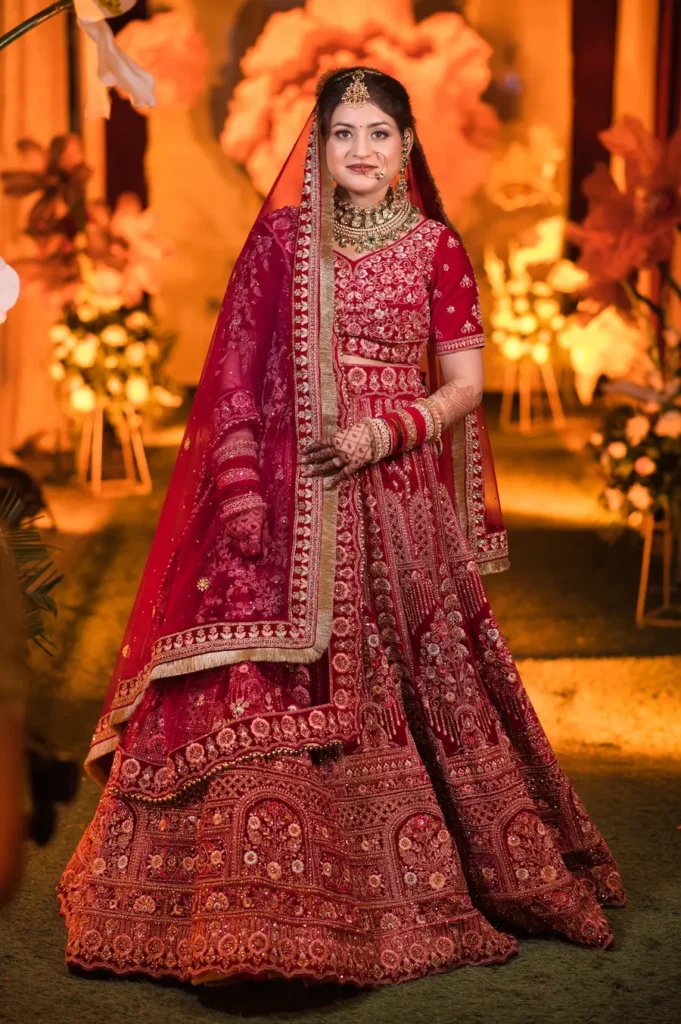 Bride in traditional red bridal attire posing with a beautifully decorated wedding venue in the background.