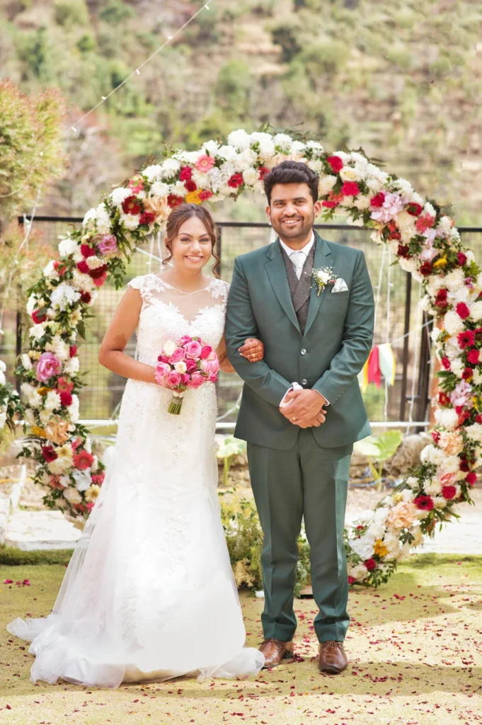 Bride and groom smiling together beneath a beautifully decorated floral wedding arch.