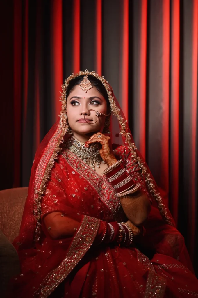 Elegant bridal portrait with dramatic lighting showcasing traditional Indian bridal makeup, jewelry, and red wedding attire.