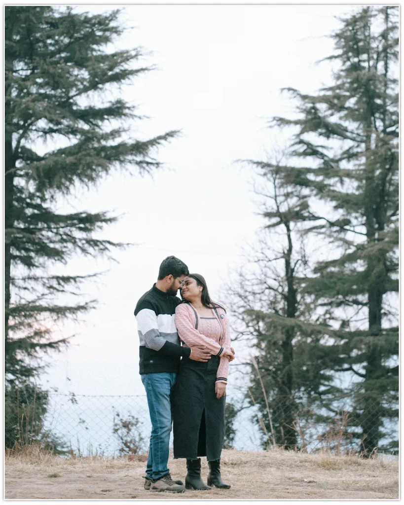 Couple sharing a quiet romantic moment among tall pine trees in a scenic mountain setting.