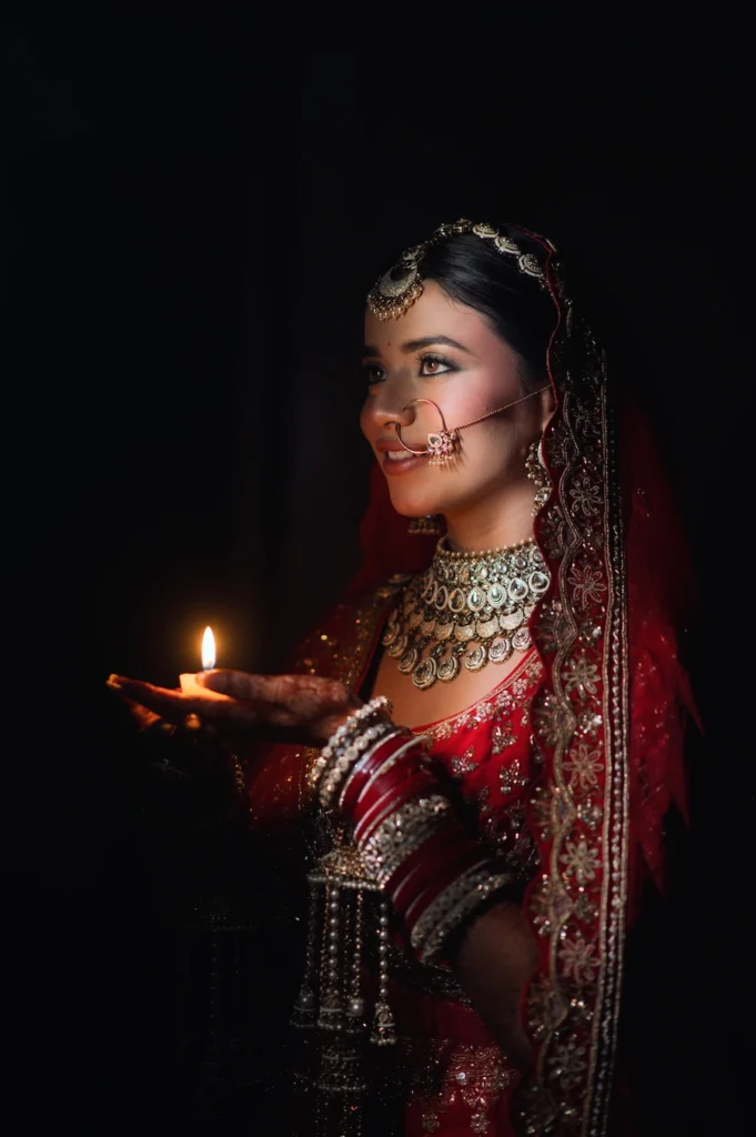 Artistic bridal portrait holding a glowing diya in soft cinematic lighting with elegant jewelry.