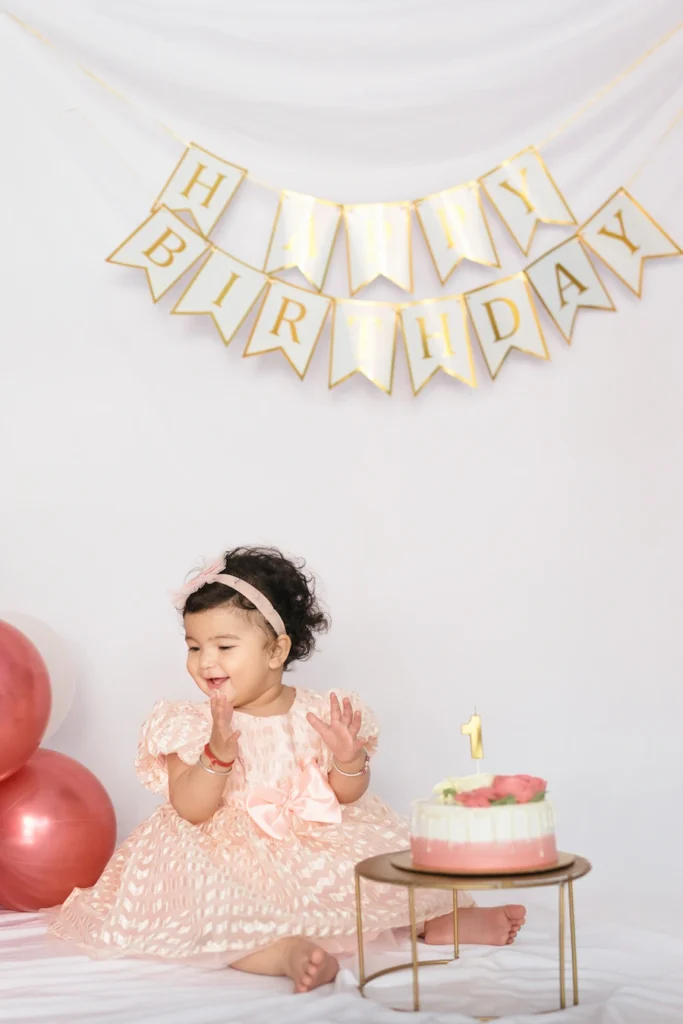Toddler celebrating with a birthday cake beneath a Happy Birthday banner in a decorated setup