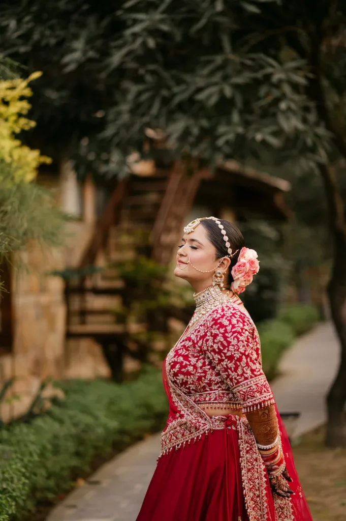 Bride posing gracefully in traditional attire surrounded by lush greenery.