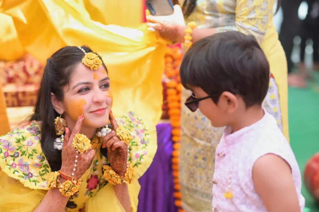 Bride smiling at a child during the vibrant Haldi celebration with floral jewelry.