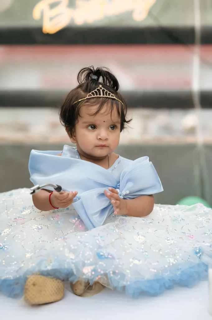 Baby girl in a blue princess gown sitting indoors during a birthday portrait session