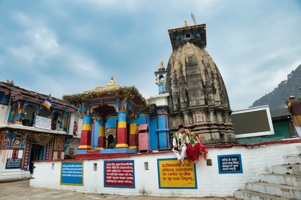 Bride and groom posing at Omkareshwar Temple during a traditional Ukhimath wedding, surrounded by vibrant Himalayan temple architecture in Uttarakhand.