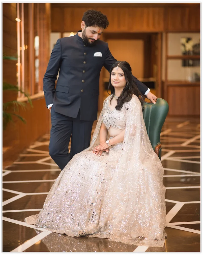 Elegant engagement portrait of the bride seated gracefully while the groom stands beside her in a beautifully lit indoor venue.