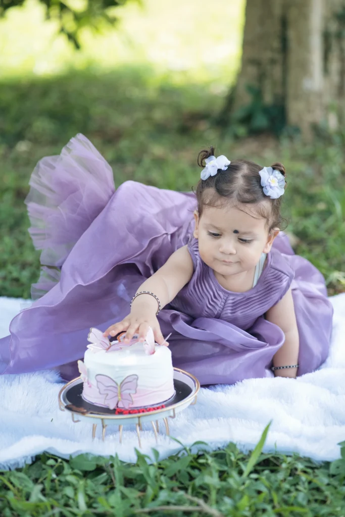 Little girl cutting a birthday cake during an outdoor celebration in a purple party dress