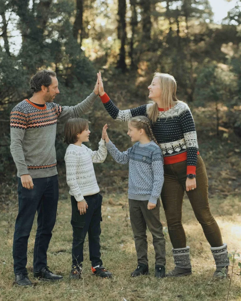 Family photoshoot in Mussoorie capturing parents and children sharing a joyful high-five in a scenic forest.