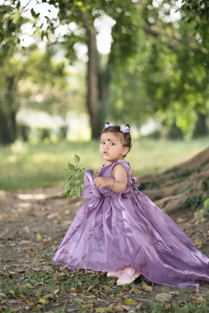 First birthday photoshoot of a baby girl in a purple princess dress walking through a park with greenery