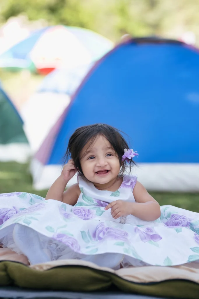 First birthday photoshoot of a smiling baby girl relaxing on a floral blanket during an outdoor picnic setup