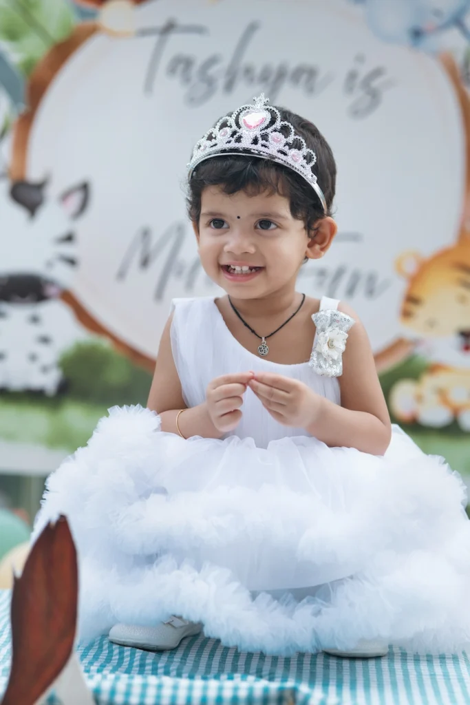Smiling toddler wearing a white princess gown and tiara during a birthday celebration