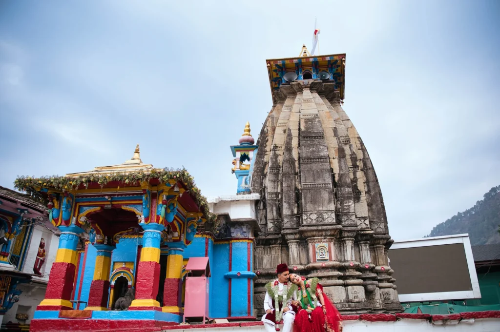 Romantic Ukhimath wedding portrait of a bride and groom seated outside Omkareshwar Temple, showcasing traditional attire and sacred wedding traditions.