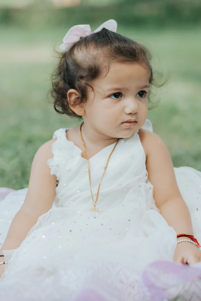 Toddler wearing a white princess dress sitting outdoors during a natural portrait session