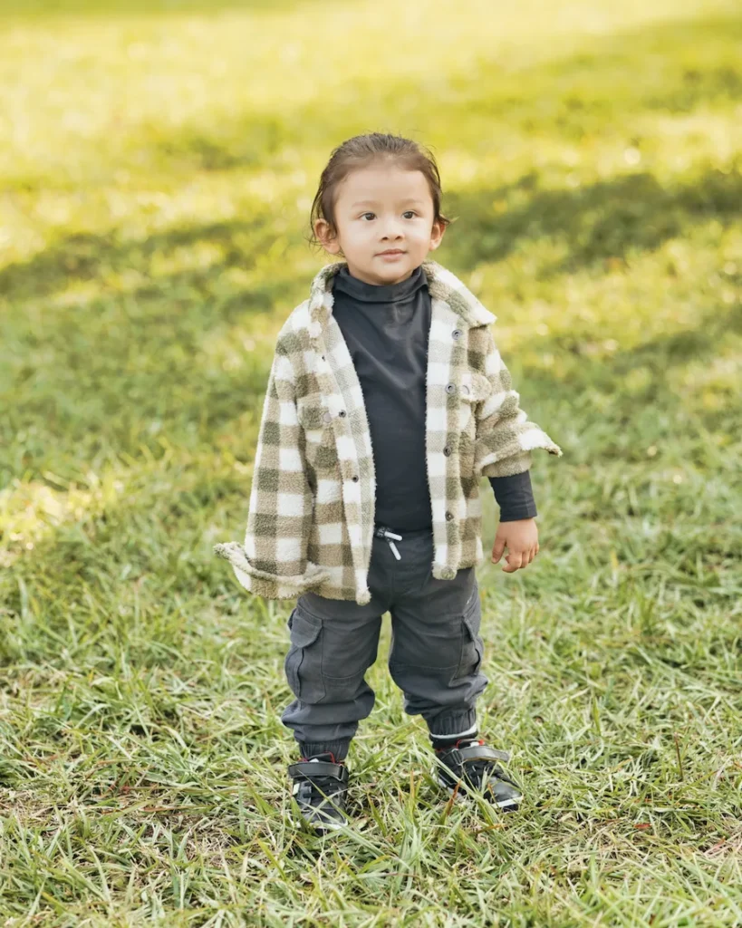 Smiling toddler standing on green grass in a casual outfit during an outdoor portrait session