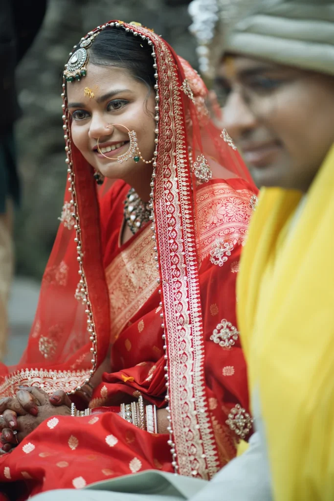 Bride smiling warmly during the sacred rituals while the groom sits beside her.