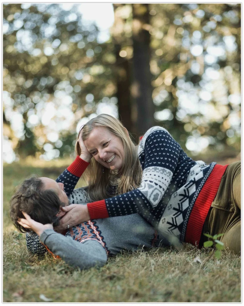 Two siblings smiling at the camera while their parents hold hands in the softly blurred foreground.