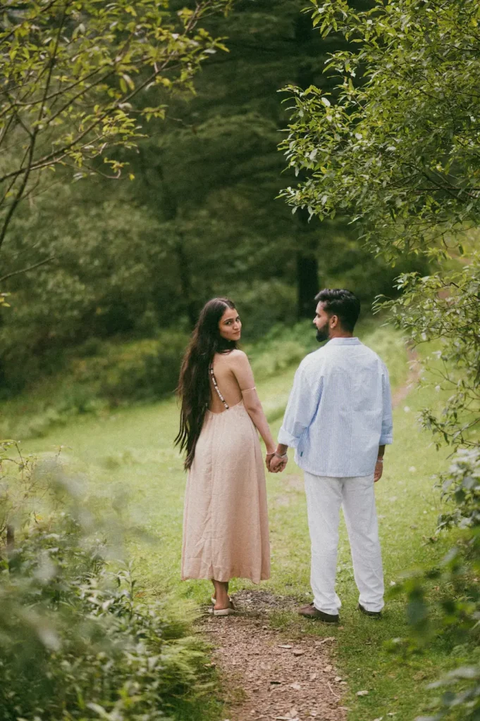 Couple walking hand in hand along a scenic forest trail surrounded by lush greenery during a romantic pre wedding photoshoot.