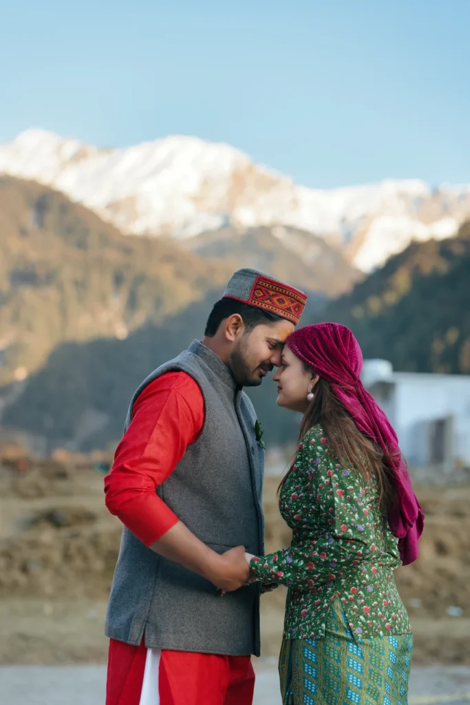 Couple wearing traditional Pahadi attire during a cultural pre wedding photoshoot with Himalayan mountains in the background.
