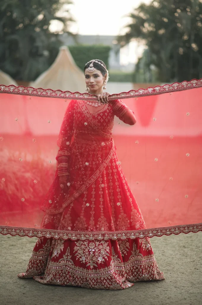 Bride posing with embroidered red bridal veil during wedding celebration
