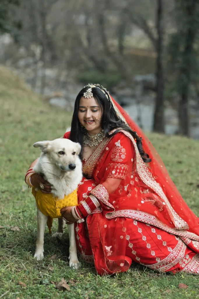 Bride in traditional red wedding attire sharing a candid moment with her pet dog before the ceremony