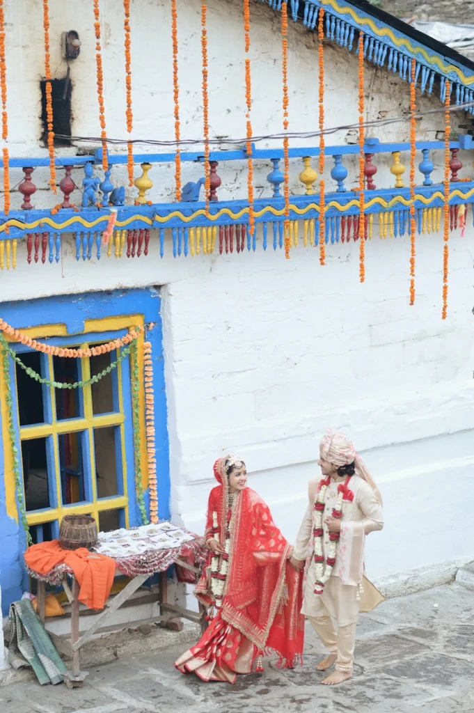 Bride and groom standing outside a decorated traditional village home during a wedding celebration