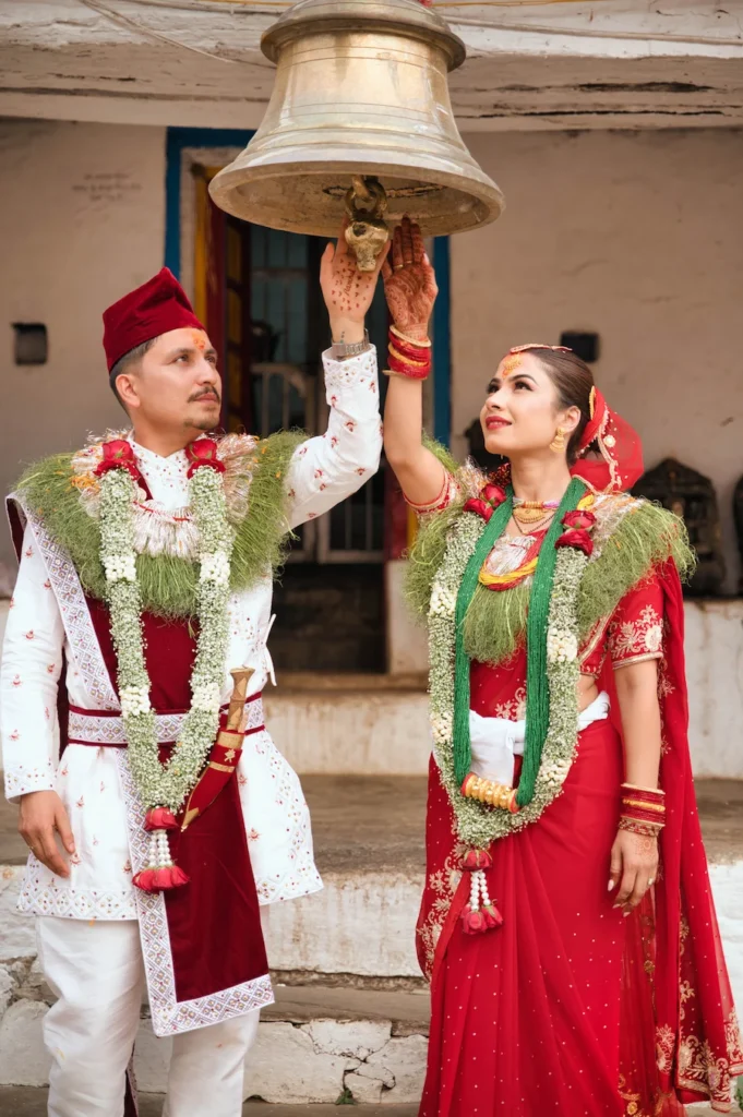 Traditional bride and groom performing a sacred wedding ritual beneath a temple bell in Uttarakhand