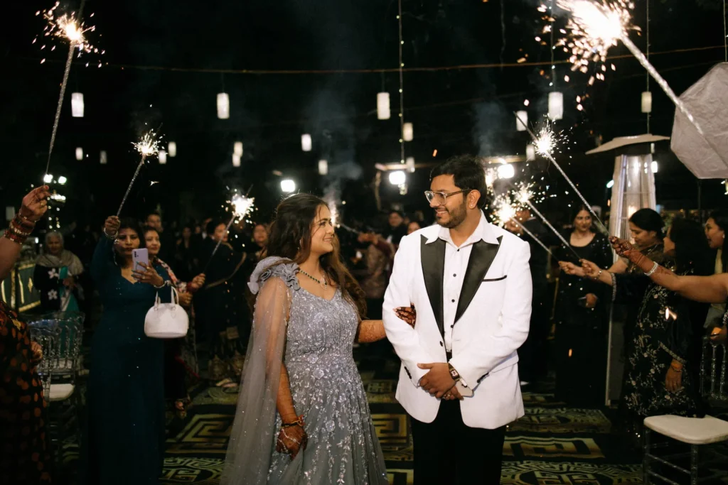 Bride and groom making a grand wedding entrance surrounded by sparklers and guests during an evening celebration