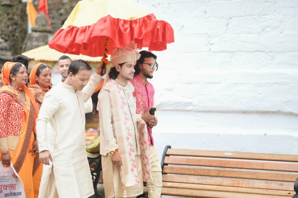 Groom walking in a traditional wedding procession under a ceremonial umbrella with family members