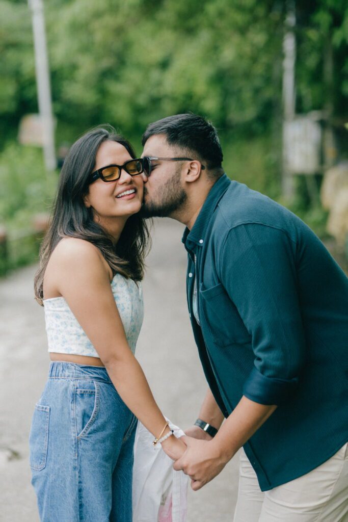 A young couple sharing a playful, intimate kiss on a scenic path in Mussoorie, captured during a relaxed pre-wedding photography session by Prism Eye Productions.