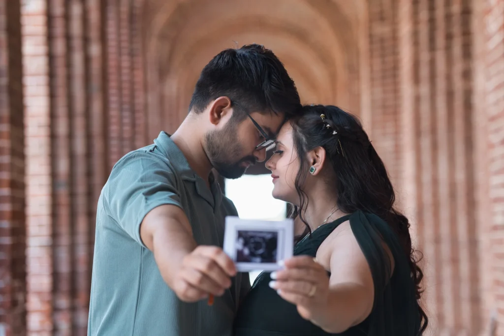 An expecting couple sharing an intimate moment in a brick corridor, lovingly holding an ultrasound scan toward the camera.
