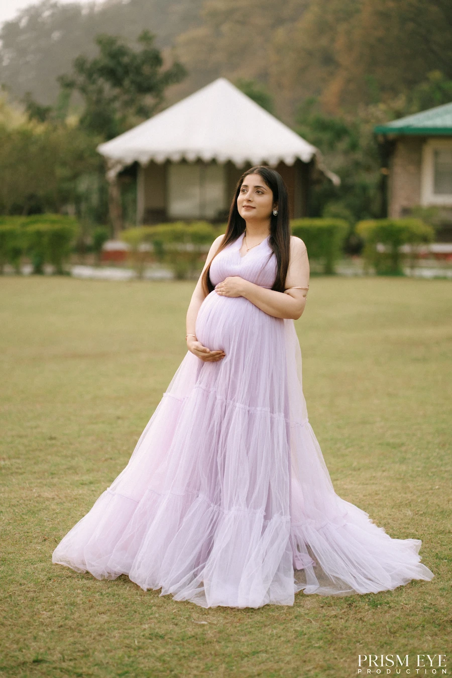 A beautiful pause to celebrate the little life growing within. Pregnant woman in a flowing lavender gown posing outdoors for a maternity portrait