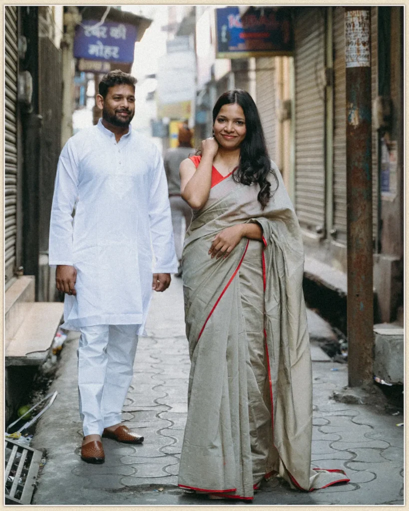 A couple dressed in traditional Indian attire walking together through a bustling, historic bazaar lane.