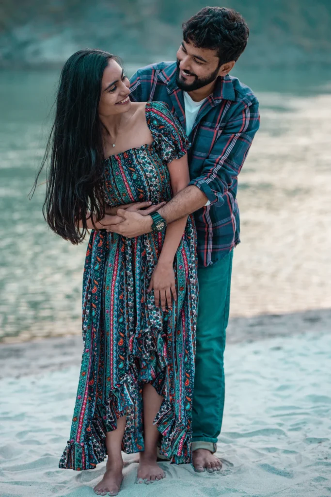 A romantic couple sharing a joyful, affectionate embrace on the sandy banks of the Ganga in Rishikesh.