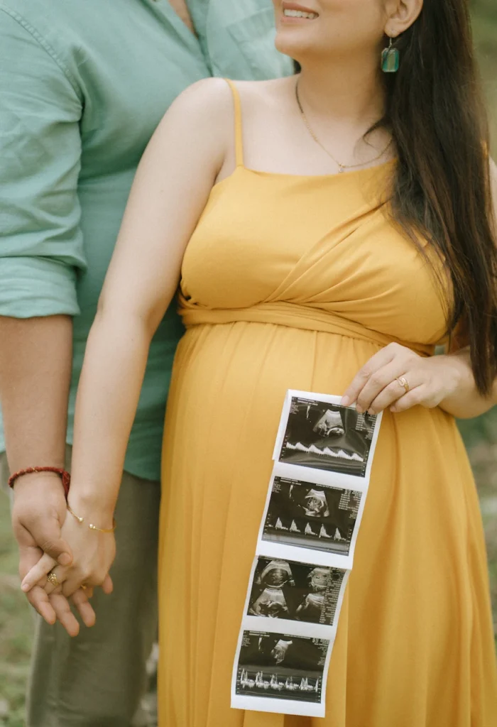 An expectant couple holding hands while the mother holds a strip of ultrasound images during a maternity photoshoot.