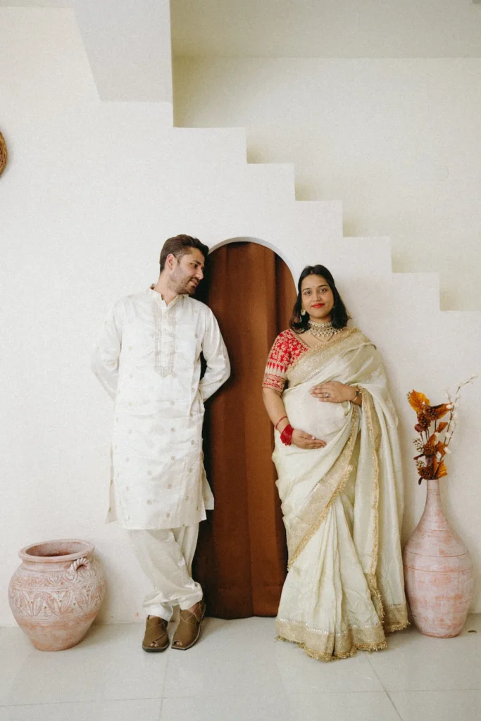 An expectant couple dressed in elegant traditional Indian attire posing for a minimal and aesthetic maternity studio portrait.