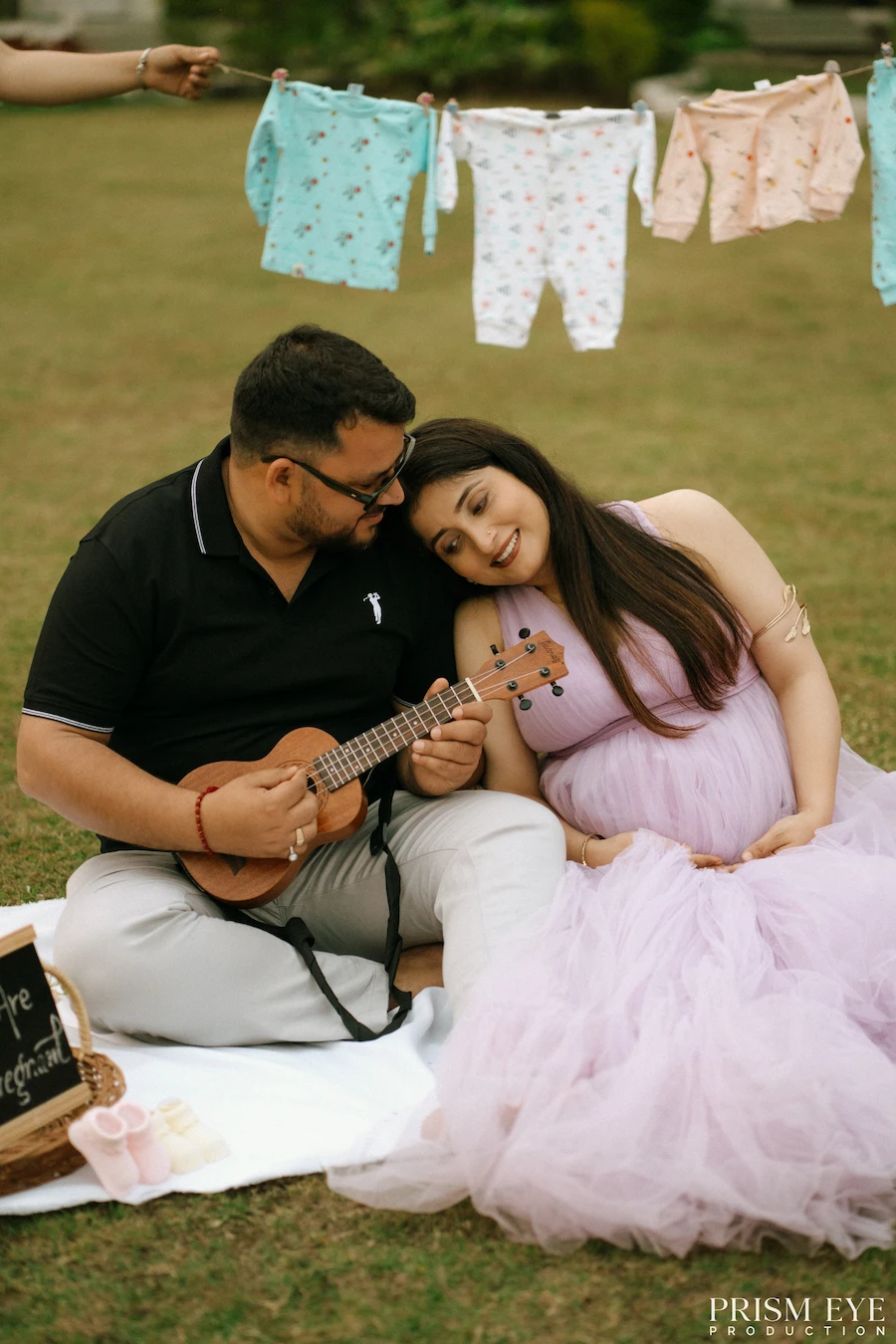 A little music, tiny clothes, and a whole lot of love waiting to arrive. Expecting couple enjoying a romantic picnic with baby clothes hanging in the background