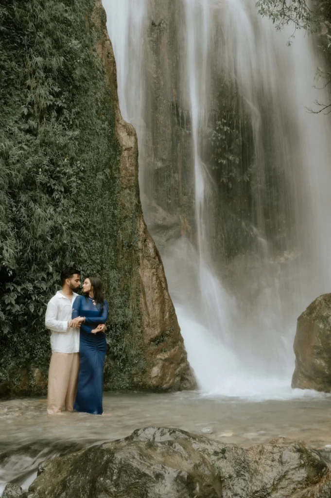 Scenic waterfall pre-wedding photography at Bhatta Falls featuring a couple surrounded by nature
