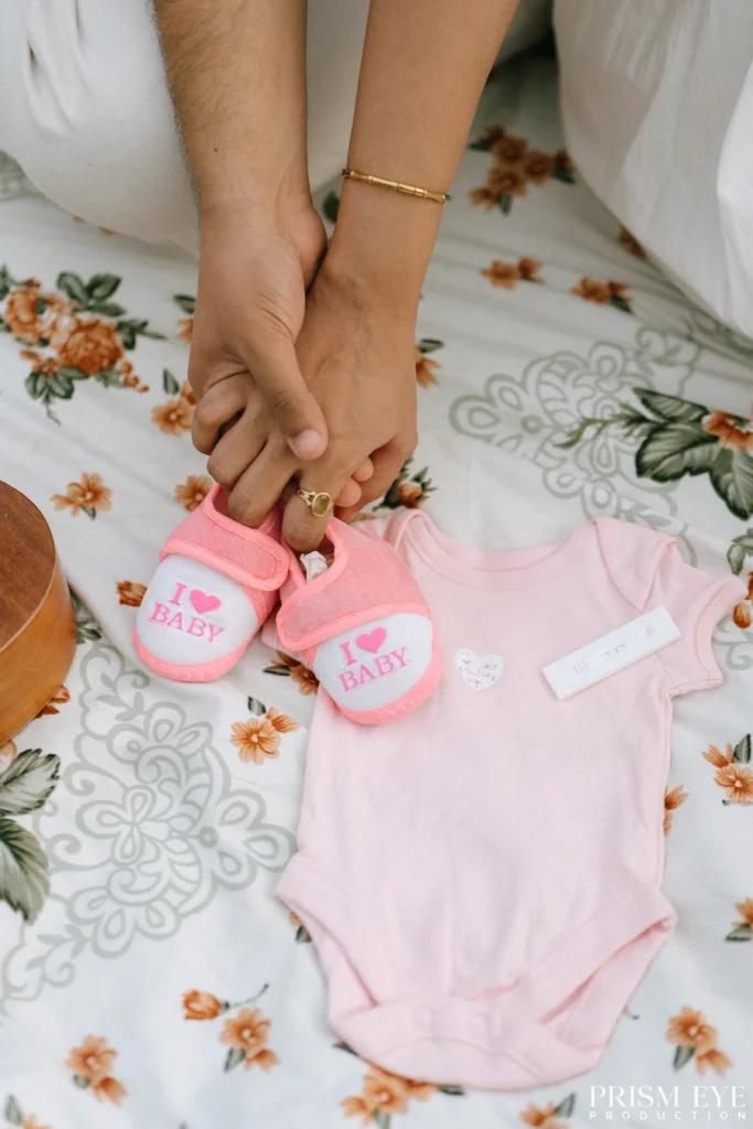 Expecting parents holding tiny pink baby shoes beside a newborn outfit