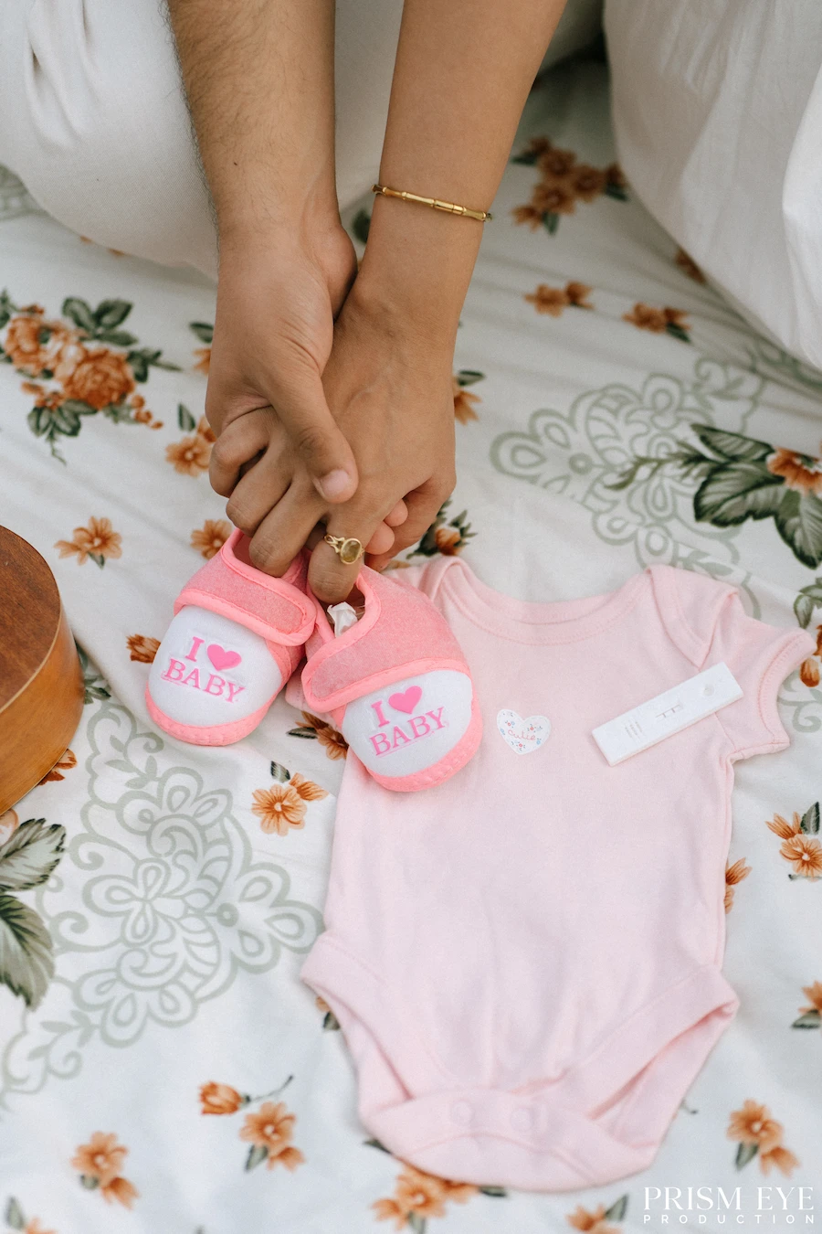 Tiny shoes, tiny clothes, and a love that already feels so big. Expecting parents holding tiny pink baby shoes beside a newborn outfit