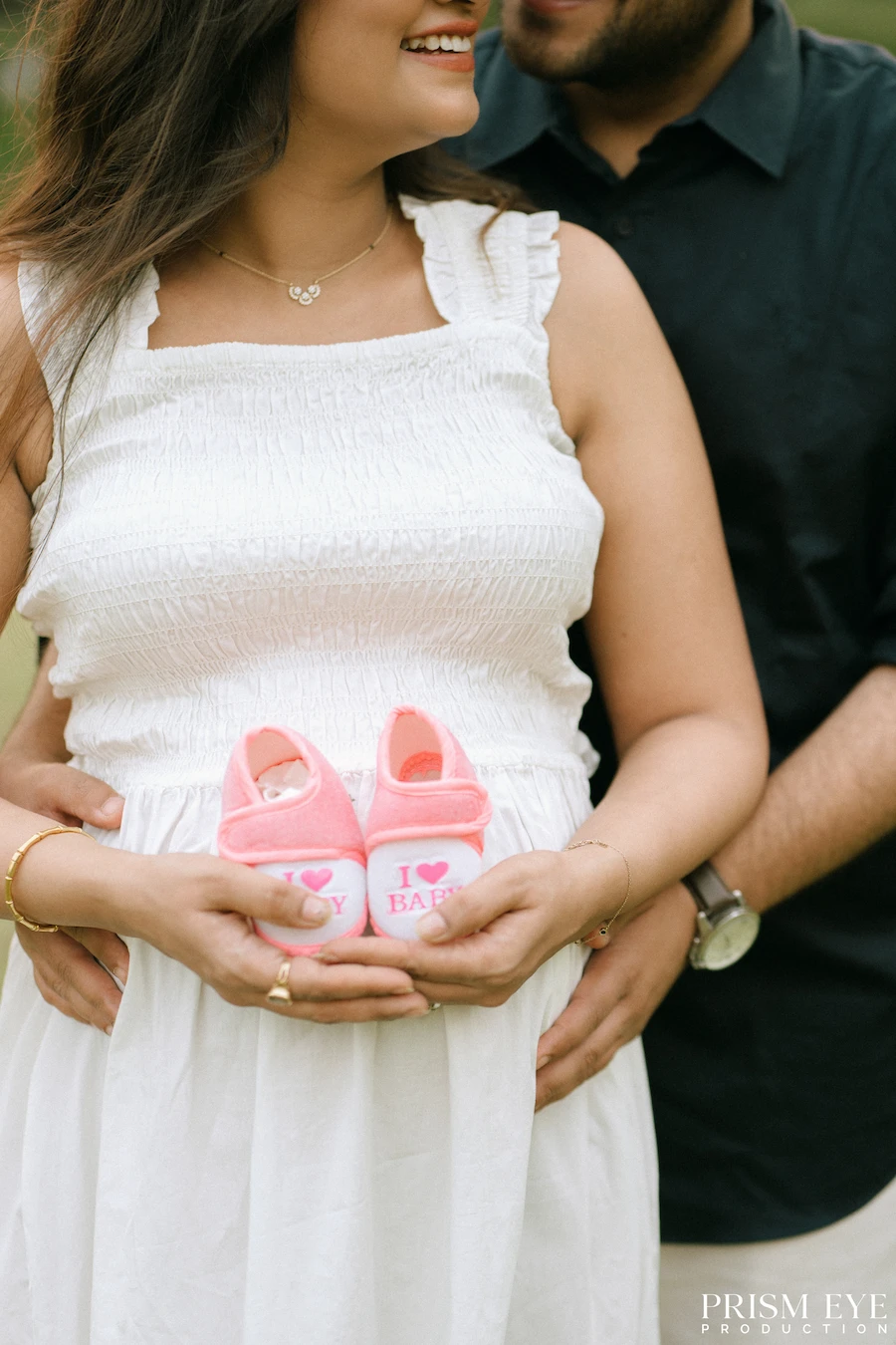 Tiny shoes, big dreams, and a whole new world of love on the way. Expecting couple holding tiny pink baby shoes during a maternity photoshoot