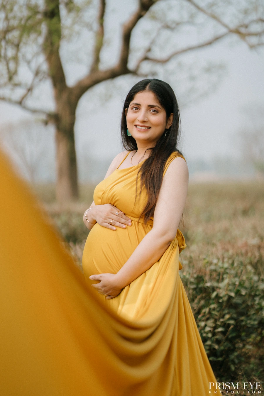 A beautiful moment celebrating motherhood, love, and the little life growing within. Pregnant woman in a yellow dress posing outdoors for a maternity portrait