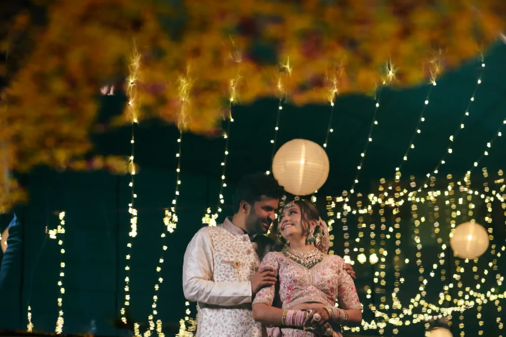 Newlywed couple posing together beneath decorative lights at their wedding reception