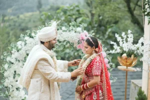 Bride and groom exchanging garlands during a traditional wedding ceremony surrounded by white flowers and greenery.