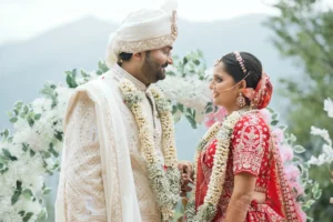 Bride and groom sharing a joyful wedding moment in traditional attire with a mountain backdrop.