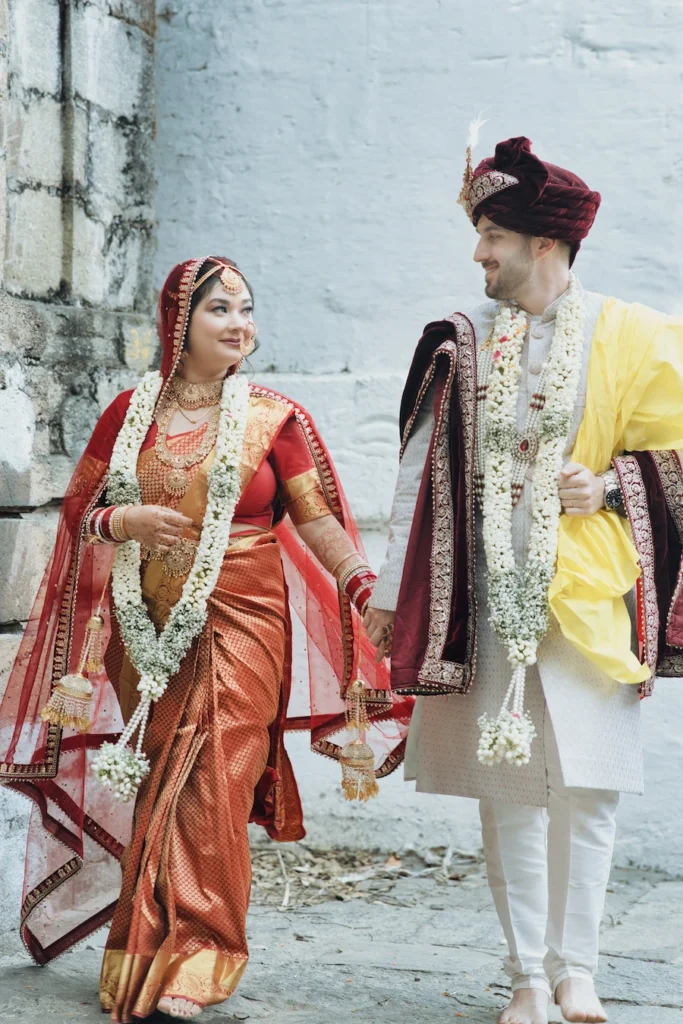 Bride and groom walking hand in hand in traditional wedding attire near a temple