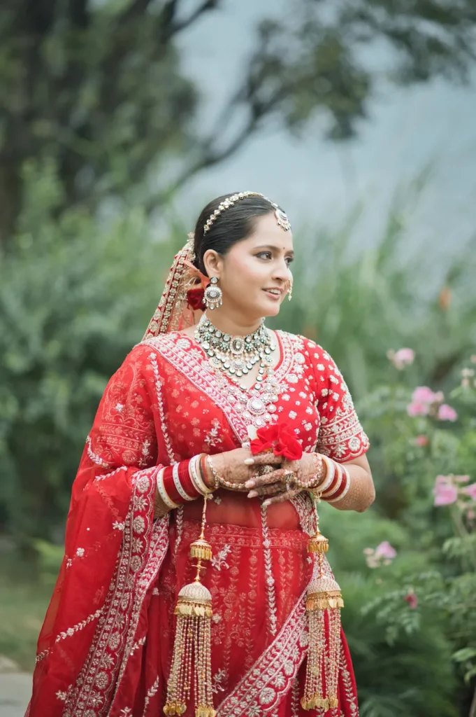 Bride in a traditional red lehenga holding flowers during an outdoor wedding portrait.